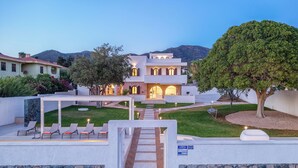 Una villa moderna con prato curato, area salotto esterna e un muro in pietra.