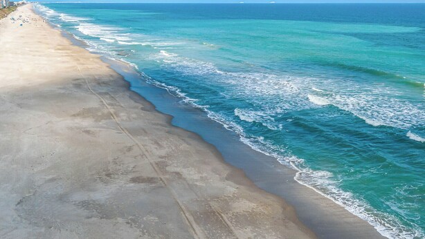 A beach with a wide sandy shore and gentle waves. - Balcony & A Patio, Private Beach Access, Heated Pool (Indialantic)