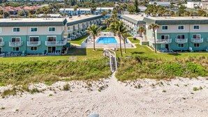 A beachfront hotel with multiple-story buildings, a swimming pool, and a sandy beach path leading to the pool. - Balcony & A Patio, Private Beach Access, Heated Pool (Indialantic)
