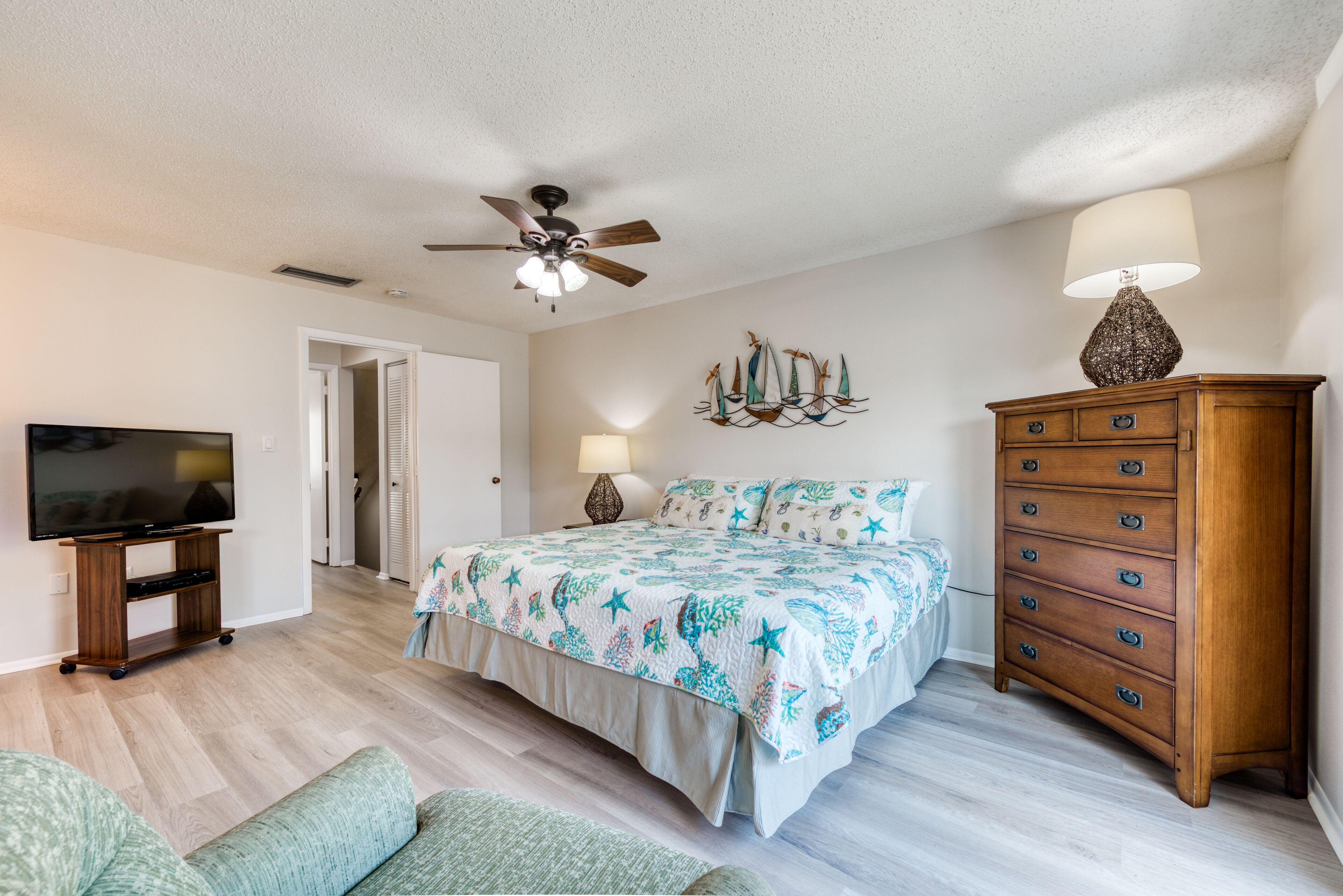 Une chambre à coucher avec un lit, une commode, un téléviseur et un ventilateur de plafond.