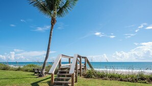 A wooden staircase leading to a beach area with a bench and a palm tree. - Balcony & A Patio, Private Beach Access, Heated Pool (Indialantic)