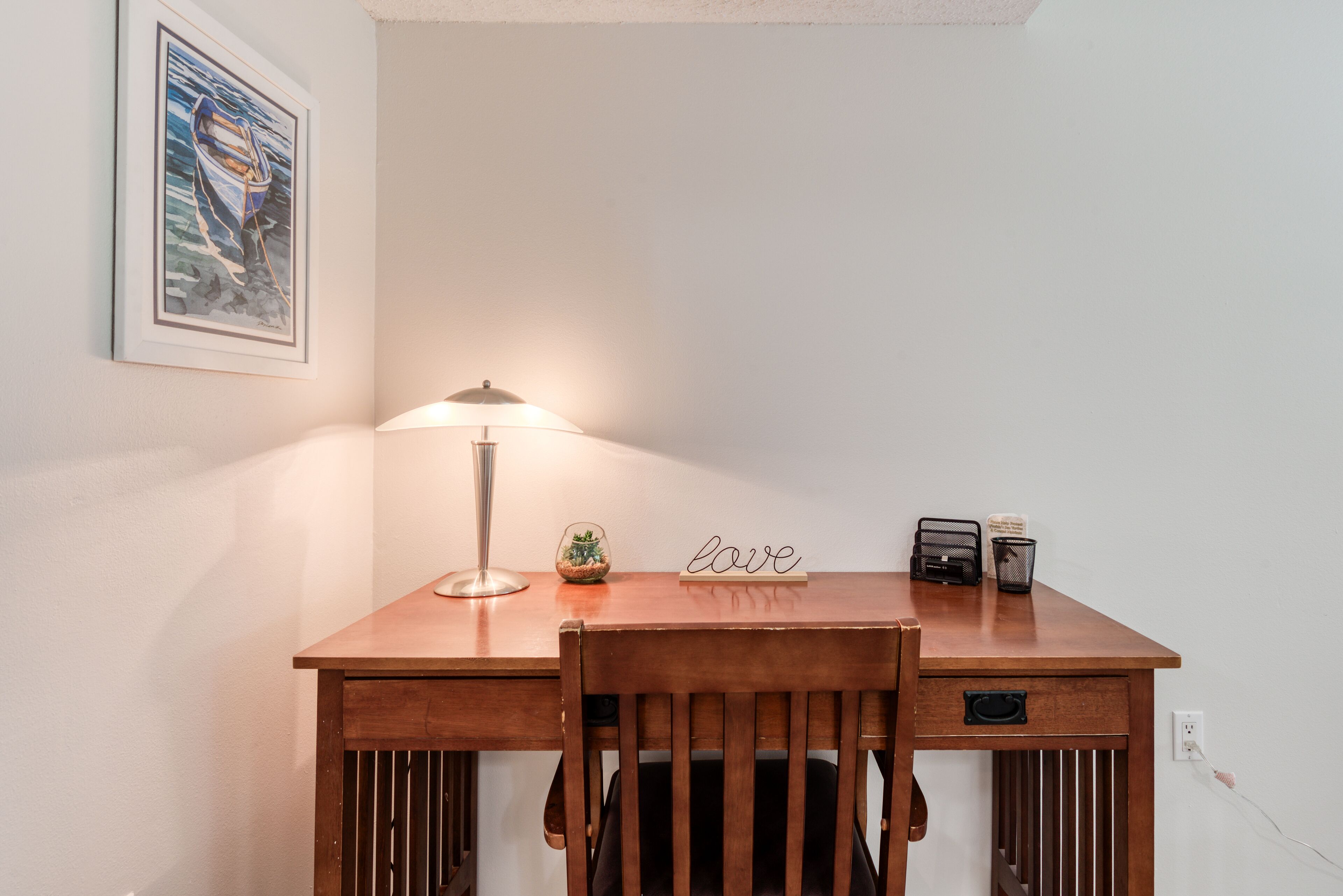 Un bureau en bois avec une lampe, une petite plante, un panneau décoratif avec le mot « amour » et un téléphone.