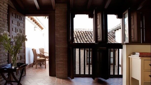 A room with a tiled floor, wooden ceiling beams, a door leading outside, and a view of a tiled roof through the door.