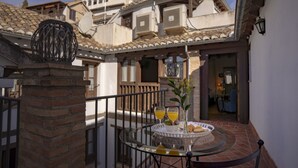 A glass table with a tray of food and drinks, a brick pillar, and a balcony with a view of buildings.