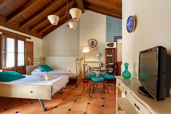 A cozy bedroom with two beds, a TV, a dining table with chairs, and a decorative plate on the wall. - Charminghomesgranada Rio Genil Apartament (Granada)