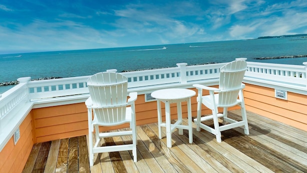 Une terrasse avec deux chaises blanches et une petite table, donnant sur une mer calme sous un ciel dégagé.