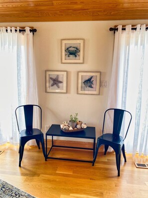 A room with two black chairs, a small table with a plant and shells, and three framed pictures on the wall.