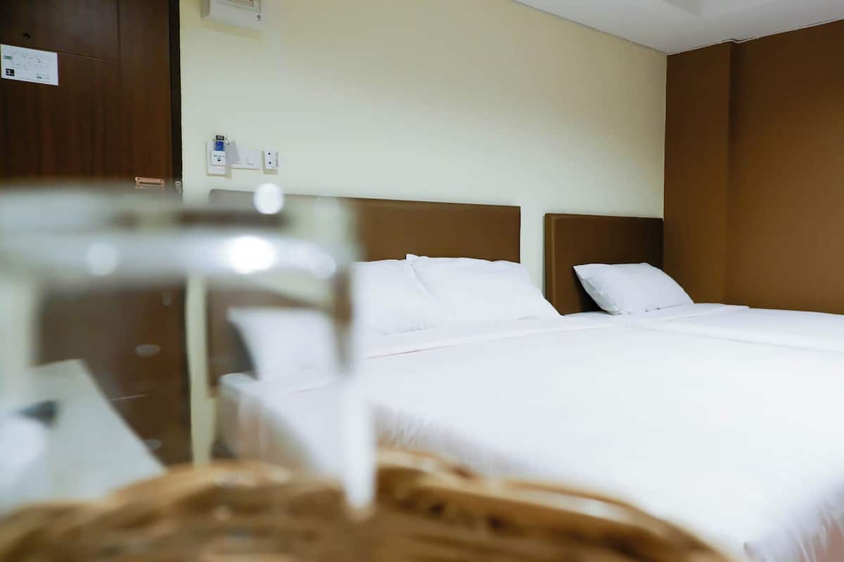 Een hotelkamer met twee bedden, een houten hoofdeinde, een witte muur en een bruine accentmuur.