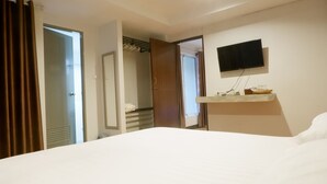 Hotelkamer met een bed, een aan de muur bevestigde televisie, een klein plankje met toiletartikelen en een deur naar de badkamer.