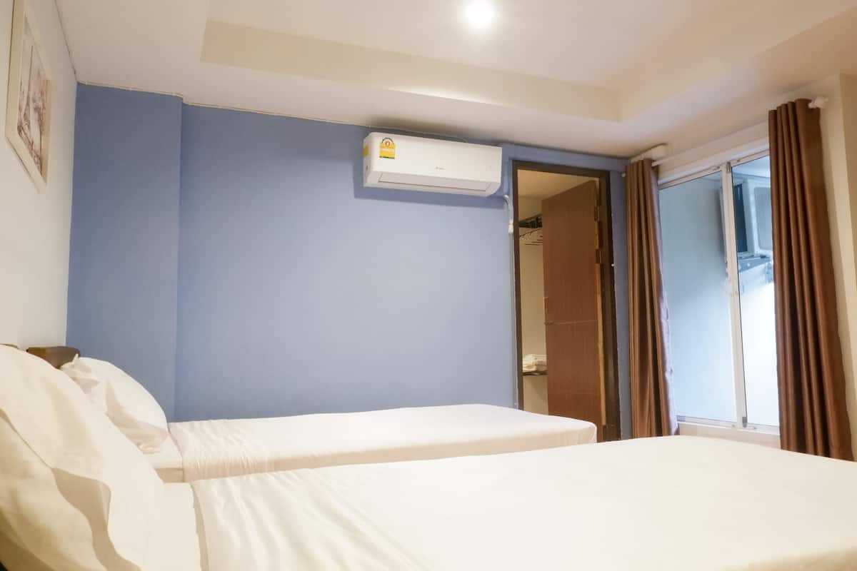 Een hotelkamer met twee eenpersoonsbedden, een raam met gordijnen, een airconditioning op de muur en een deur naar een badkamer.
