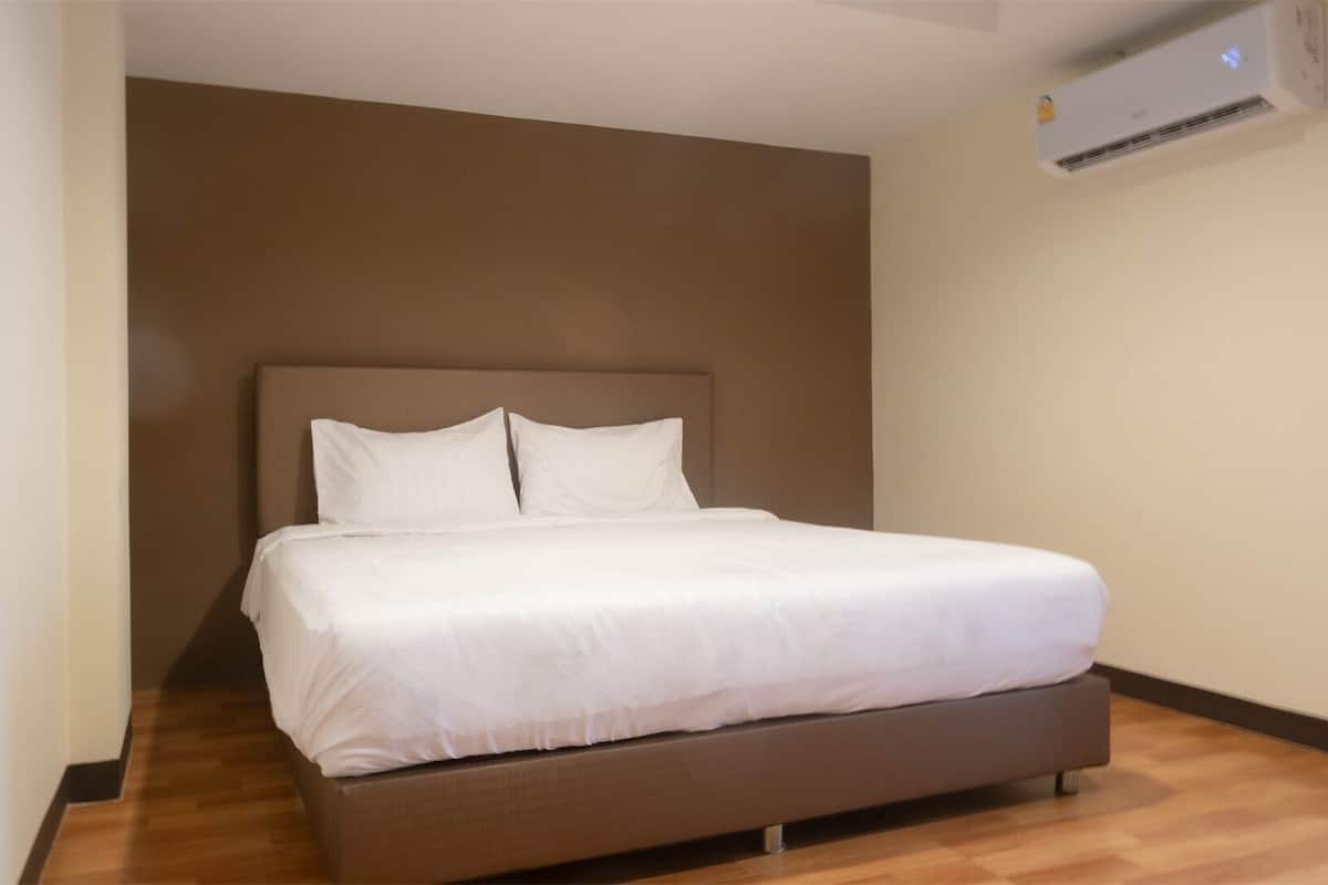 Een enkel bed met hoofdbord, witte beddengoed en een houten vloer.