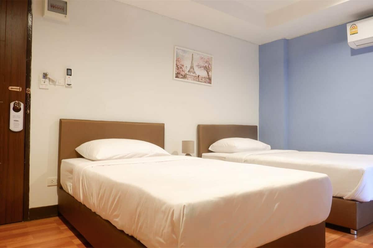 Een hotelkamer met twee bedden, een houten vloer, een wandairconditioner en een deur met slot.