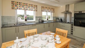 A modern kitchen with a dining area, featuring a large window, stainless steel appliances, and a table set for tea. - 2 Sunny Hill (Haverfordwest)