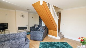 A living room with a wooden staircase, a TV, a fireplace, and a green rug. - 2 Sunny Hill (Haverfordwest)