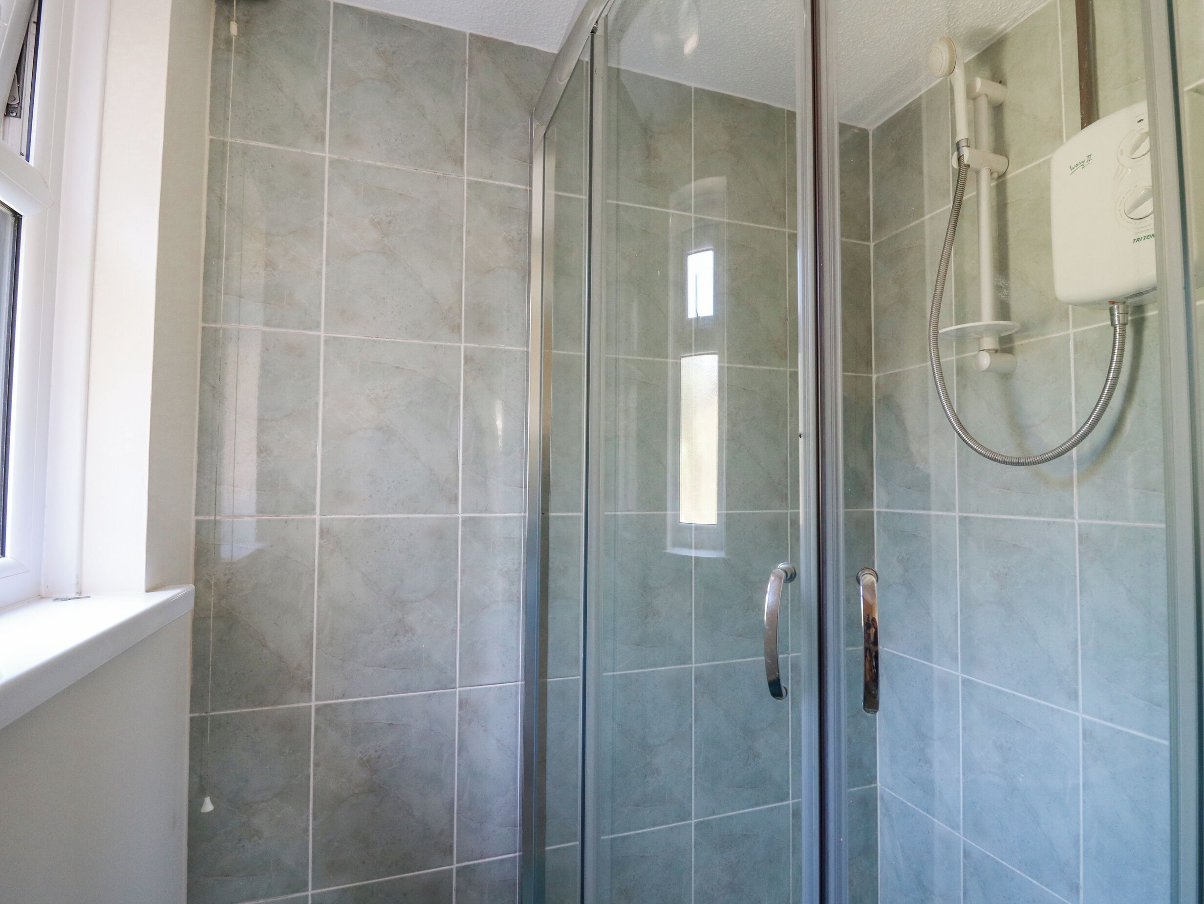 A glass-enclosed shower with a handheld showerhead and a wall-mounted control panel.