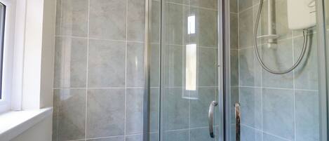A glass-enclosed shower with a handheld showerhead and a wall-mounted control panel.