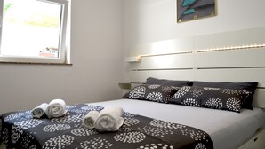 Un lit bien fait, recouvert d’une couvre-lit à motifs, avec deux oreillers à pois et une fenêtre dont les stores sont partiellement ouverts.