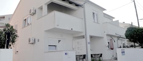 A two-story residential building with a balcony, a small outdoor seating area, and a visible number '18' on the wall.