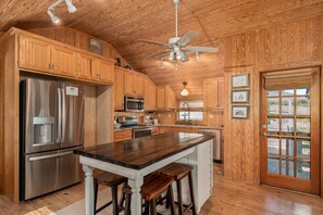 A kitchen with wooden cabinets, a stainless steel refrigerator, a ceiling fan, and a large island with stools.