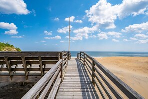 A wooden boardwalk leading to a sandy beach with a clear sky.