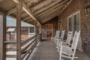A wooden porch with a railing, a door, and several rocking chairs.