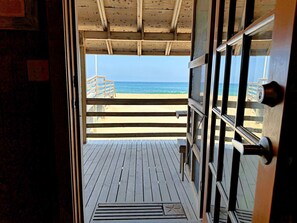 Una puerta de madera abierta que da a una terraza de madera con vista a la playa y al océano.