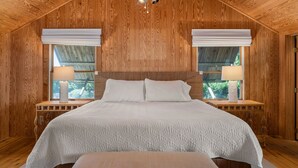 Ett sovrum med träpanel på väggarna, en stor säng, två sänglampor och en takfläkt.