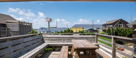 Een houten terras met banken en picknicktafels, met uitzicht op een kustgebied met gebouwen en een heldere lucht.