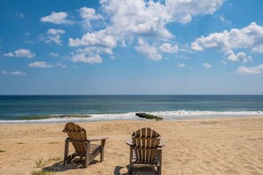 Una playa con dos sillas de madera tipo Adirondack mirando al océano.