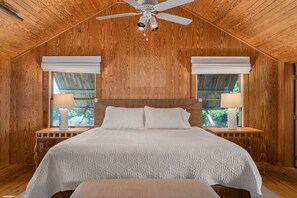 A wooden-paneled bedroom with a large bed, two bedside lamps, and a ceiling fan.