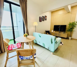 A modern living room with a sofa, a TV, a small table with a lamp, and a chair with a cushion. - Stunning Seaview Cosy Studio Apartment In Melaka (Malacca City)