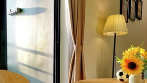 Een kamer met een stoel met een kussen van Chelsea Football Club, een tafel met een lamp en een bloemenvaas, en een raam met gordijnen.