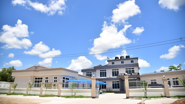 Un hotel con fachada moderna, un acceso cubierto y un cielo azul despejado con nubes.