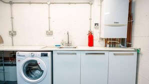 A laundry room with a front-loading washing machine, a sink, and a red fire extinguisher.