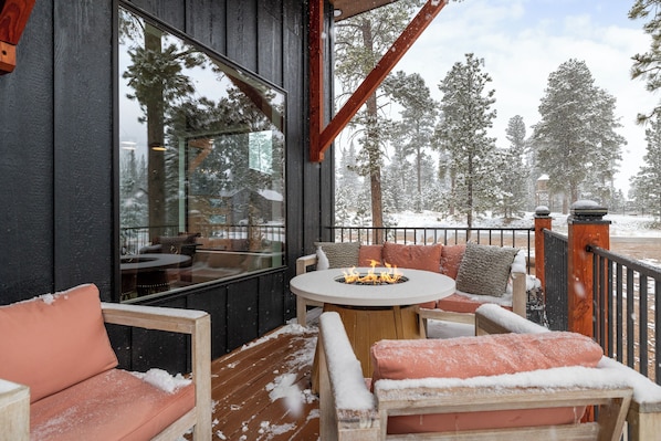 Une terrasse en bois avec un foyer, des sièges et une vue sur des arbres couverts de neige.