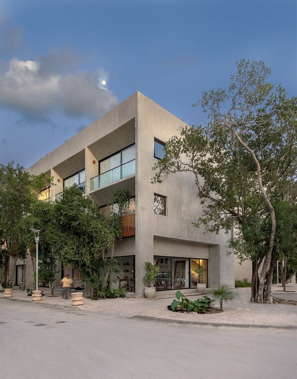 A modern building with multiple floors, large windows, and a courtyard with plants and a tree. - Unbeatable Located 2 Br Apt With Amazing Natural Lig (Tulum)