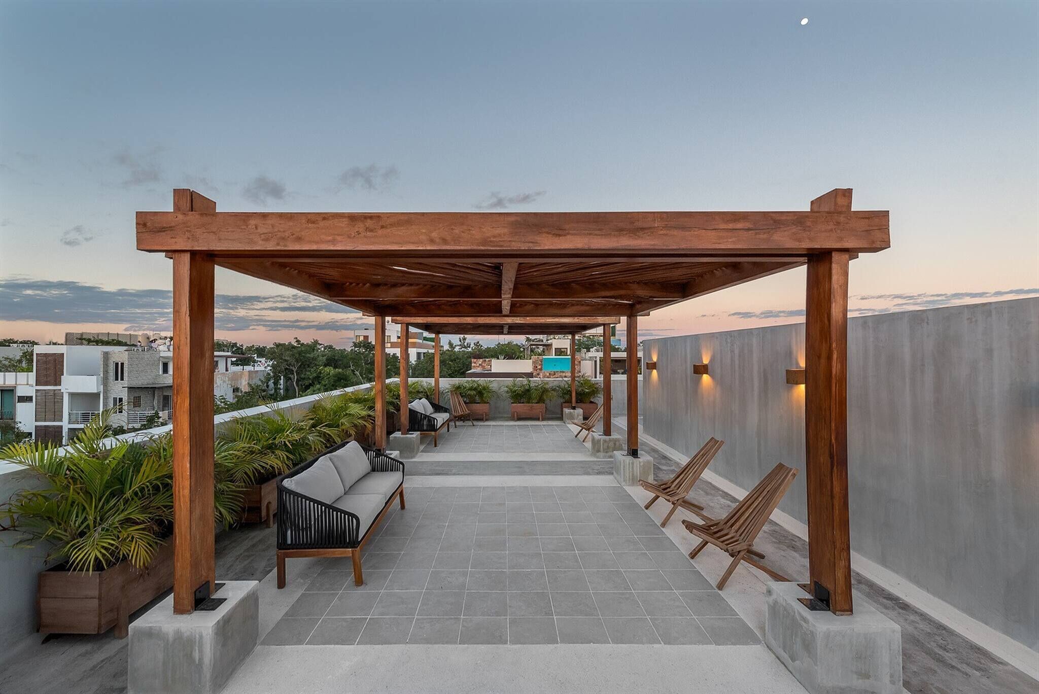 Un área de estar al aire libre techada con una pérgola, plantas en macetas y vistas de la ciudad.