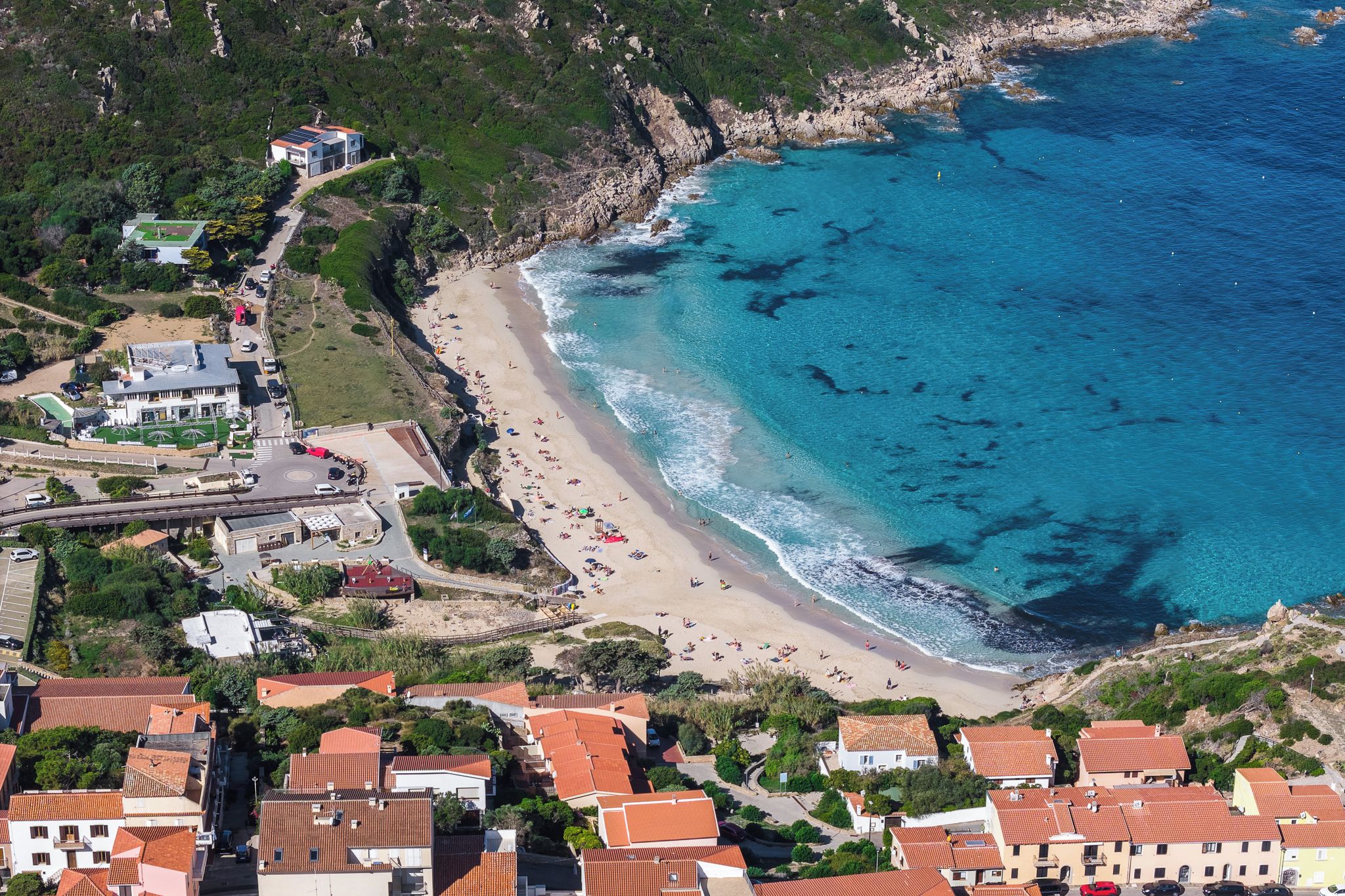 An aerial view of a coastal area with a beach, buildings, and a rocky coastline.
