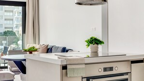 A modern kitchen with a built-in oven, a small dining area with a table and chairs, and a large window with a view of buildings. - Sanders Premier - Cozy 2 bdr apt With Balcony (Limassol)