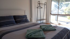 Een net opgemaakt bed met een gestreept dekbed en twee opgevouwen groene handdoeken.
