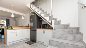 A modern kitchen with white cabinets, a stainless steel refrigerator, and a microwave. There is a staircase with grey steps leading to another level. - Apartments Peaceful Place (Stanici)