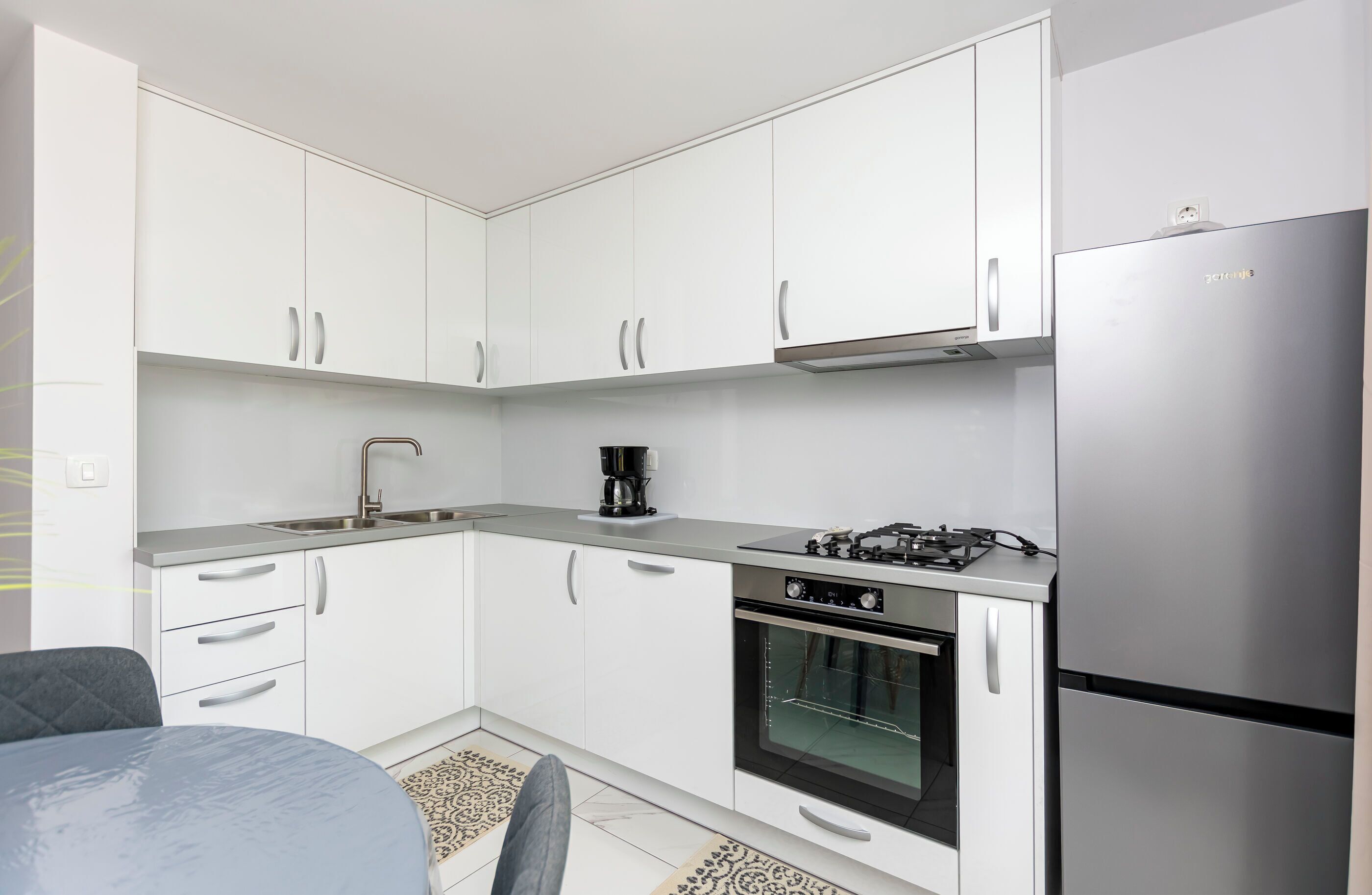A compact kitchen with white cabinets, a gas stove, an oven, and a stainless steel refrigerator.