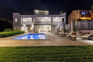 A modern two-story house with a swimming pool, outdoor seating, and a well-lit entrance. - Villa Srdella (Podstrana)