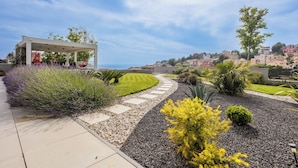 Un jardin aménagé avec une pergola, un sentier sinueux et une vue sur une ville côtière.