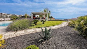 Un espace extérieur moderne, aménagé avec des sièges confortables et une piscine, entouré d’un jardin bien entretenu et offrant une vue dégagée sur la mer.