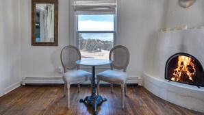 A room with a fireplace, a table with two chairs, a window with a view, and a wall-mounted mirror. - Tesuque Outpost |3 Casitas |Best views in Santa Fe (Santa Fe)