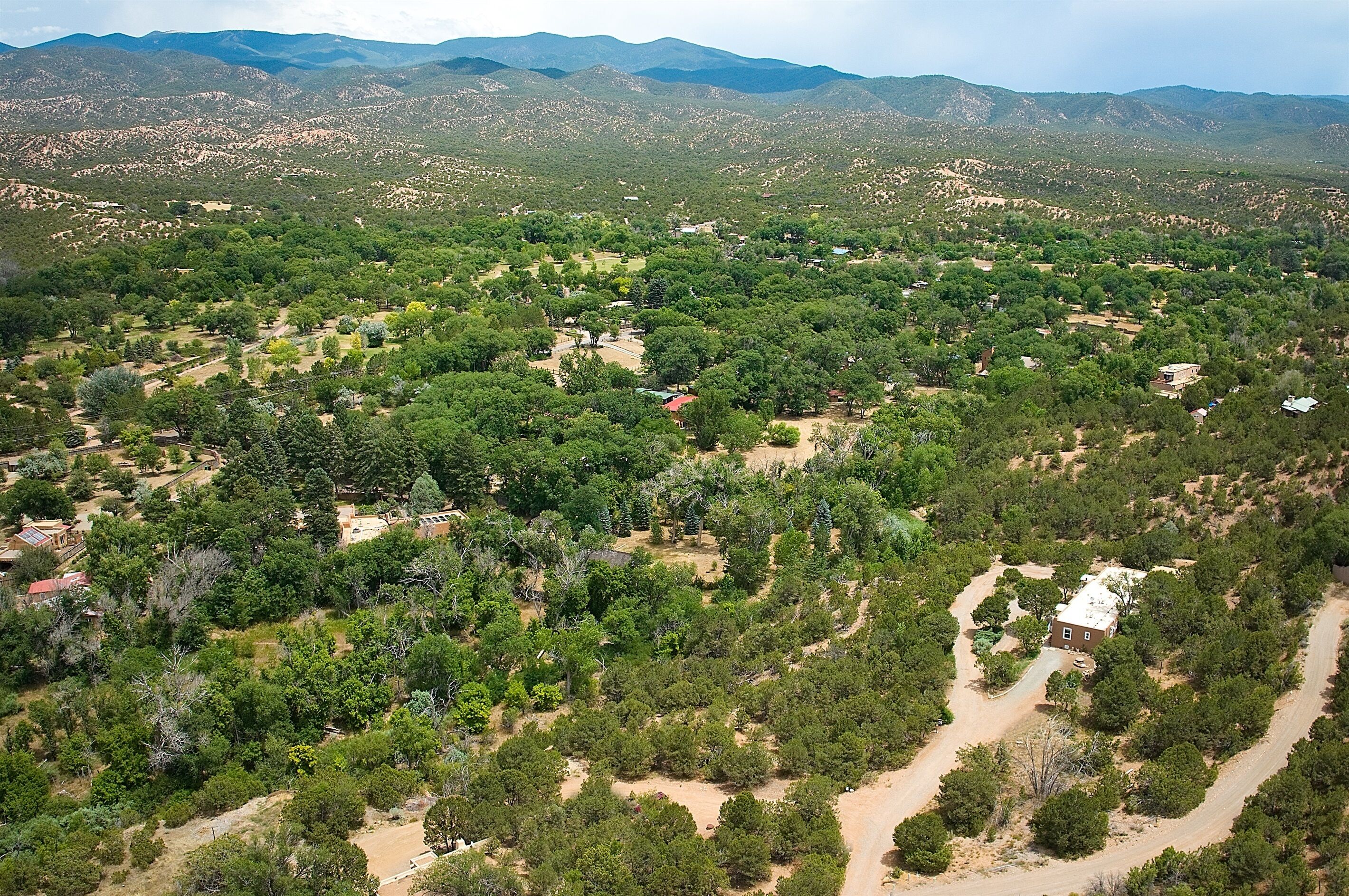 An aerial view of a rural area with scattered houses surrounded by dense vegetation and mountains in the background.