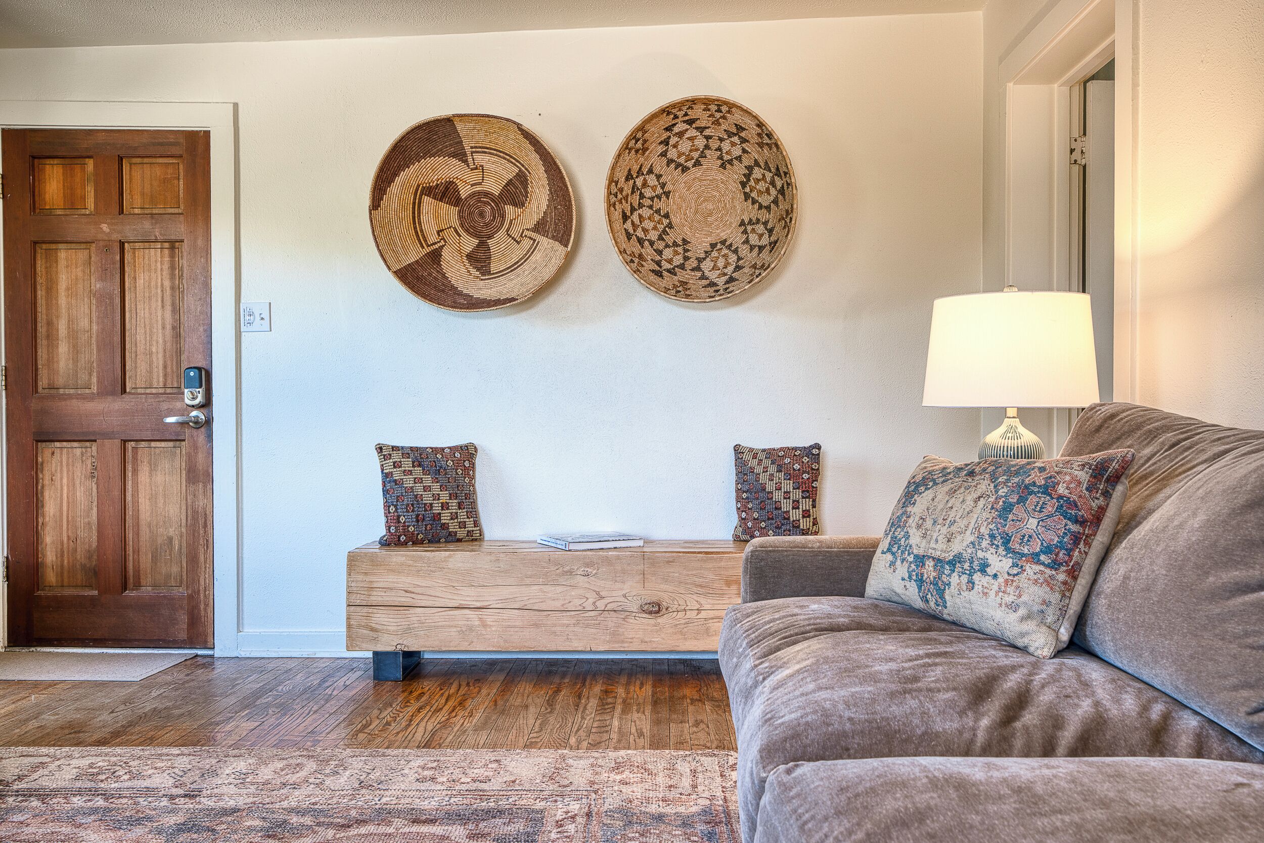 Una sala de estar con un banco de madera, dos tapices decorativos, un sofá marrón y una lámpara.
