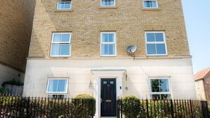 A multi-story building with a brick facade, multiple windows, a satellite dish, and a black front door. - Stunning 6-bed House in Milton Keynes (Milton Keynes)