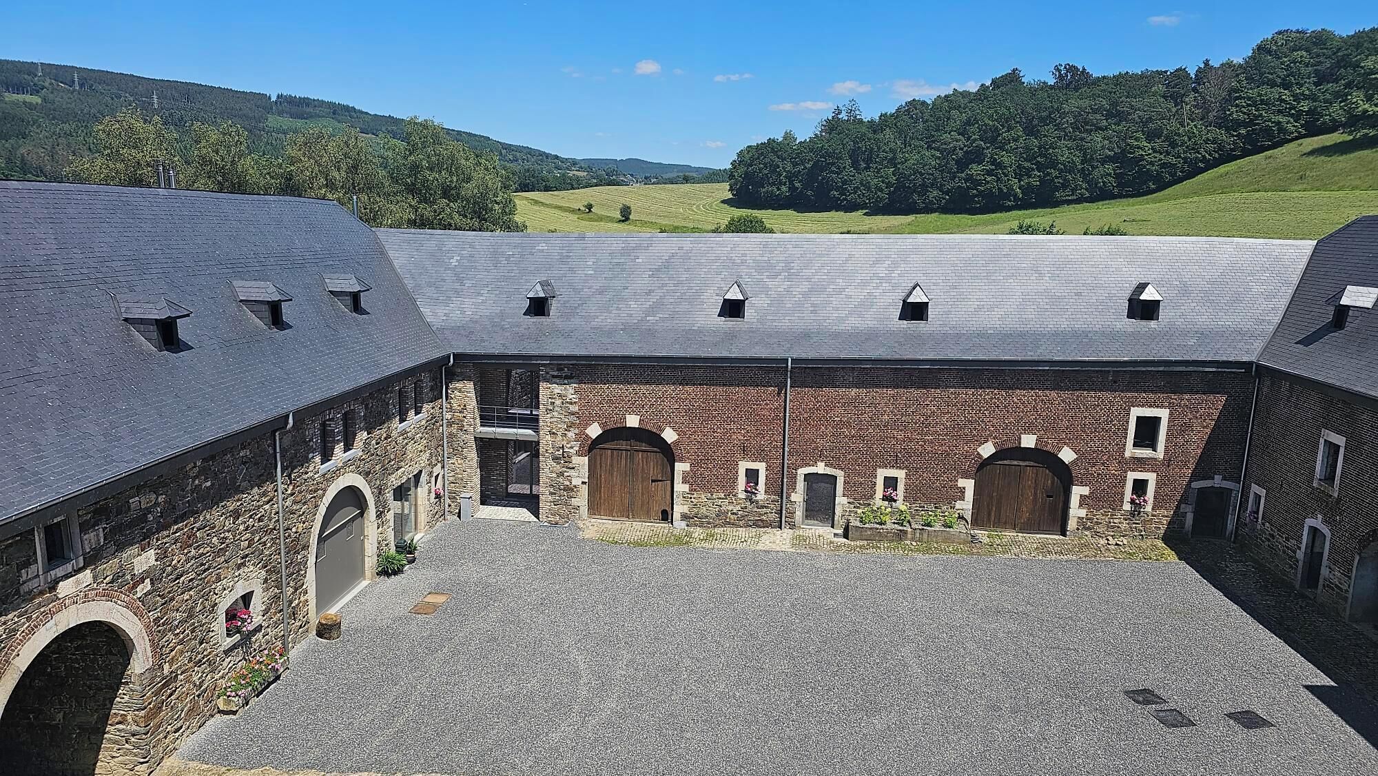 A courtyard with stone walls, a brick building with arched doorways, and a sloped roof.